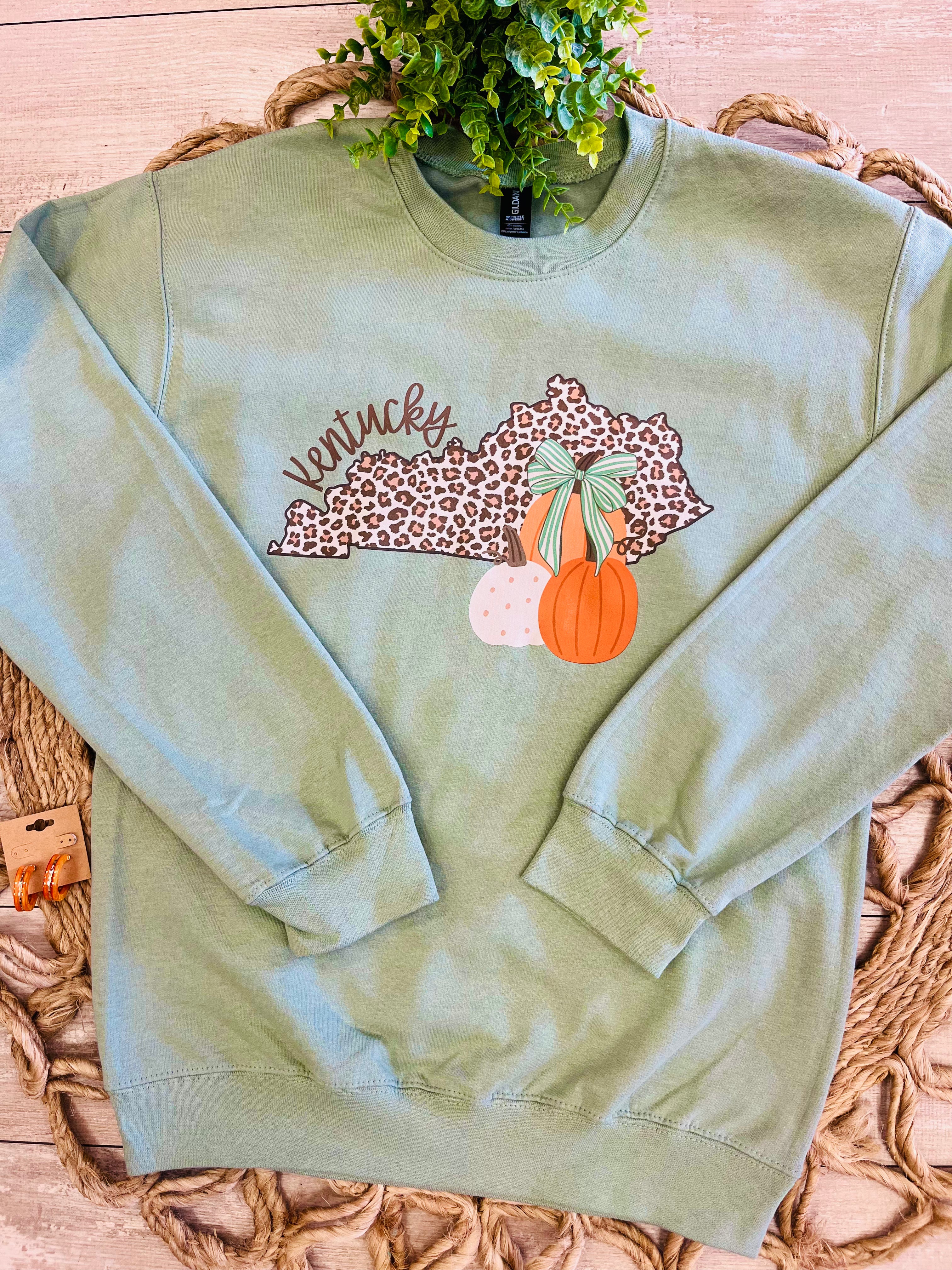 Women’s Sage Green Crewneck Features a cute Leopard - Print outline of Kentucky paired with stacked Autumn Pumpkins